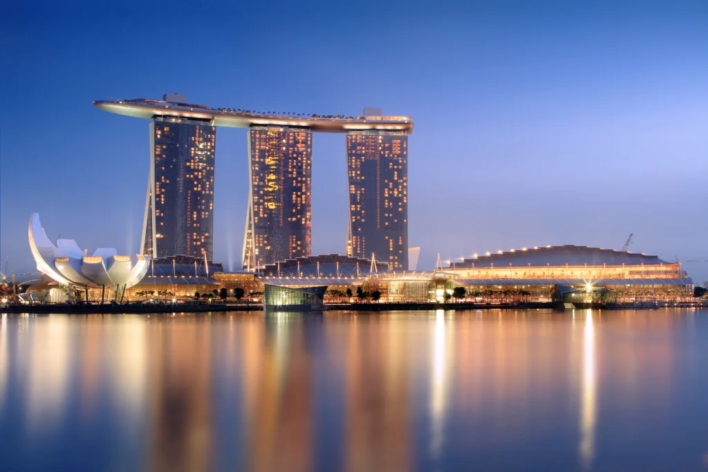 Marina Bay Sands integrated resort in Singapore at dusk, showing the three hotel towers, SkyPark, waterfront reflections, and ArtScience Museum.