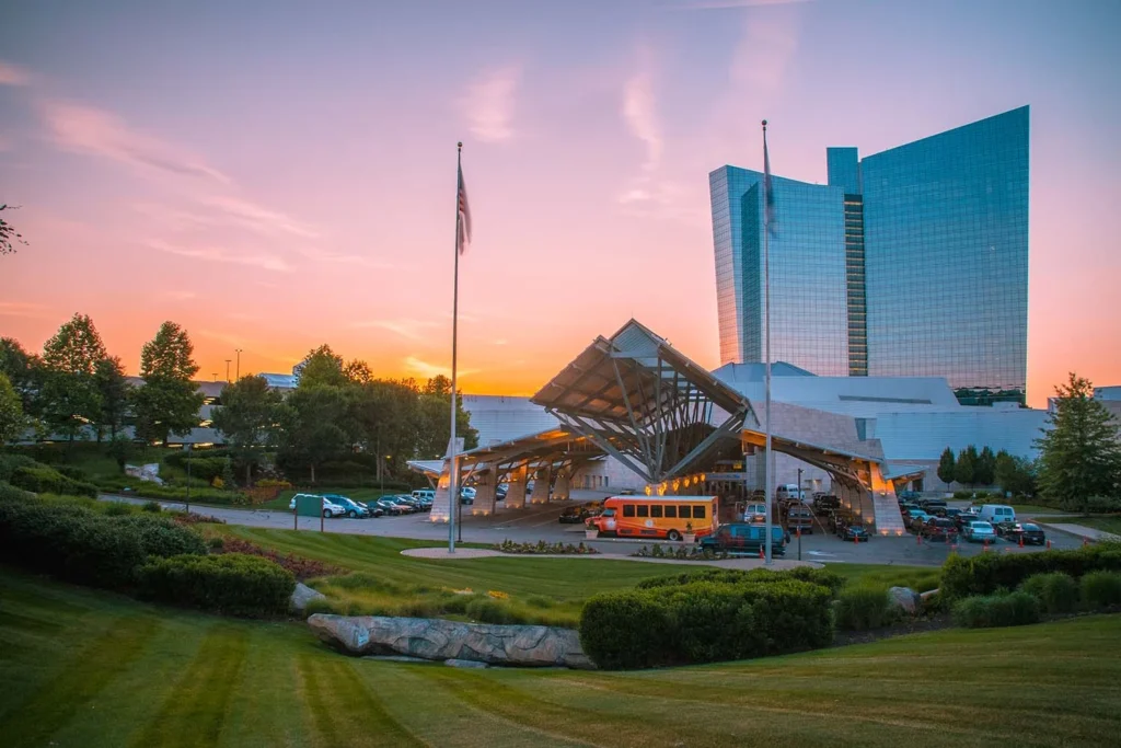 Mohegan Sun casino resort entrance in Uncasville, Connecticut, with the glass hotel tower, landscaped grounds, and sunset sky.