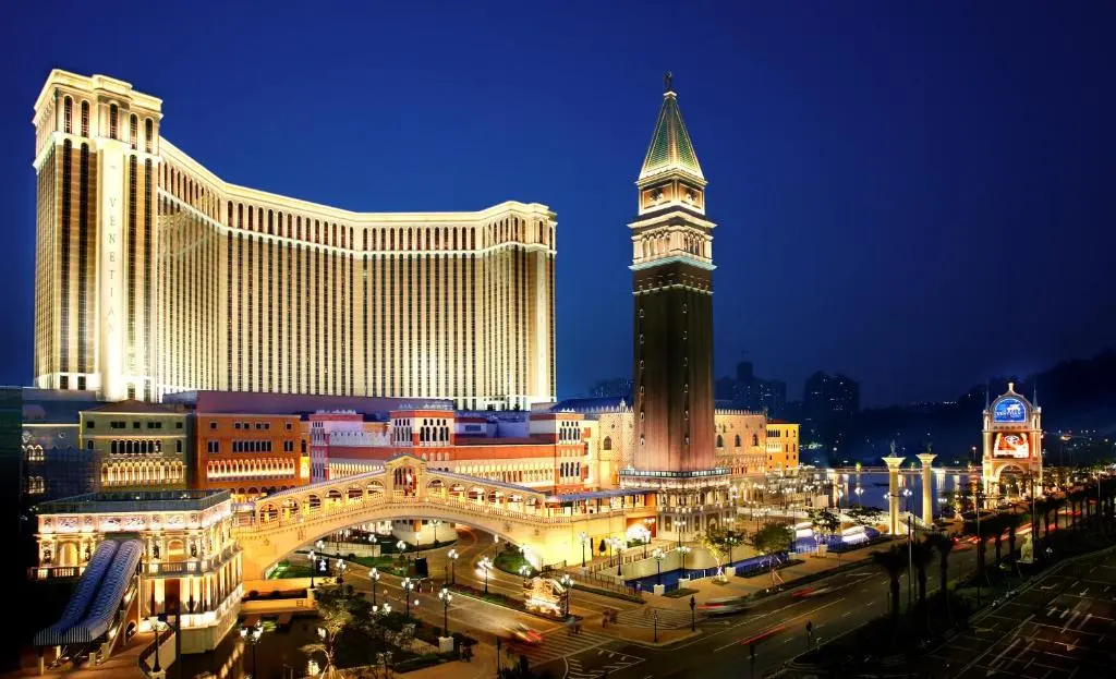 The Venetian Macao exterior at night on the Cotai Strip, showing the illuminated hotel tower, canalside architecture, and replica bell tower.